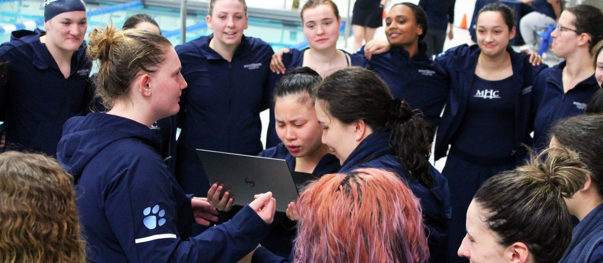 Surrounded by their teammates on Senior Day, seniors Erin Schrama and Anais Magner (center) speak remotely with senior teammate Lauren Leese via a laptop prior to Mount Holyoke's meet against Simmons University on Jan. 21, 2023.