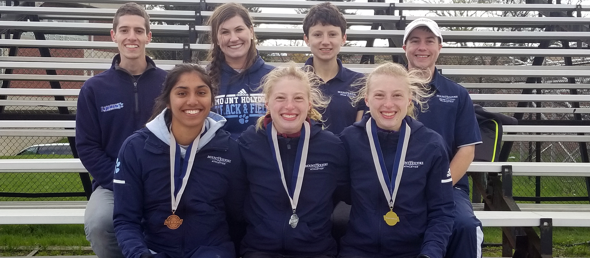 NEWMAC Medalists (Front Row) right to left: 10000m champion Hannah Rieders, 10000m runner-up Madeline Rieders, 1500m third place Simone Jacob. Back row featuring Mount Holyoke coaches.